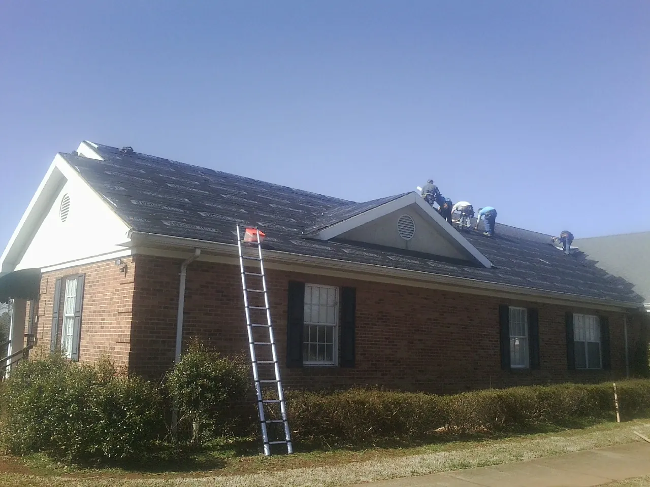 Crew tearing shingles off a brick ranch roof with a ladder set — Emergency Roof Repair work by our crew in Todd