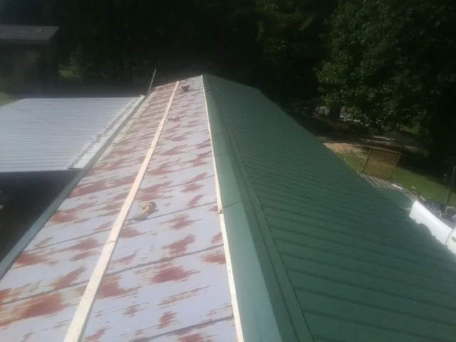 Old rusted panels beside newly installed green metal roofing — Wind Damage Roof Repair by Roofing Brothers in Todd