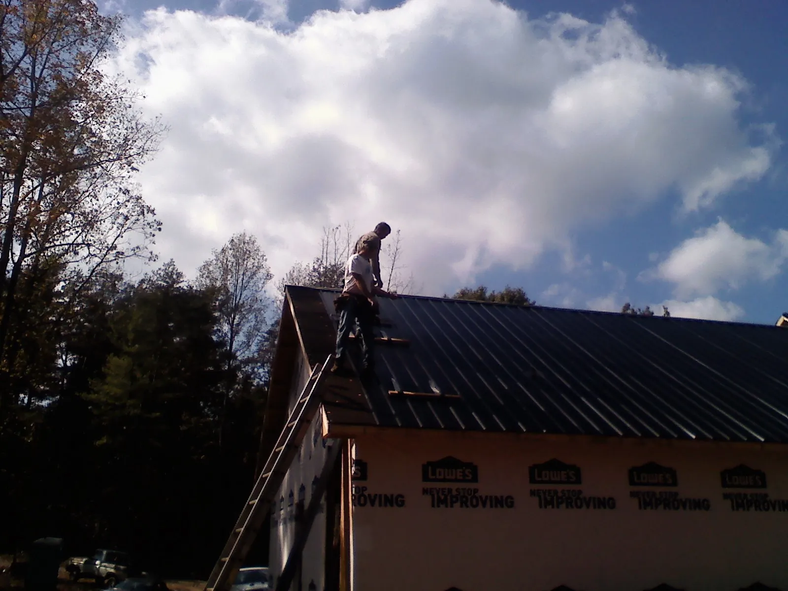 Roofer fastening dark metal panels high against a cloudy sky, from a Roof Inspection job in Todd