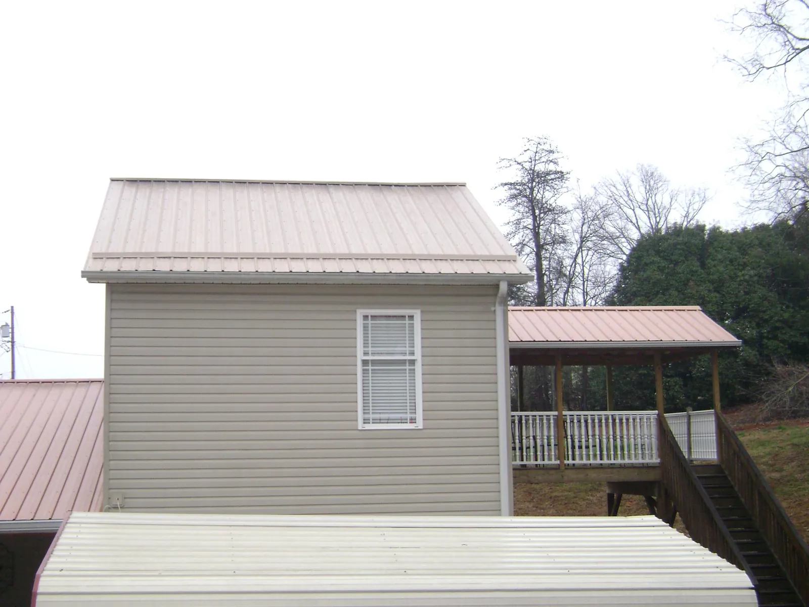 Tan metal roofs on a two story addition and attached porch, from a Roof Replacement job in Todd
